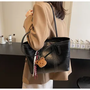 Black leather tote bag detail showing contrast stitching, bear charm, and shoulder strap.