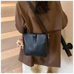 Vue détaillée d'un sac seau élégant en cuir synthétique noir avec bandoulière et charm en peluche.