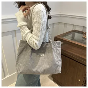 Detailansicht der grauen Cord-Tasche mit strukturiertem Stoff, Metallkette und Label-Patch.