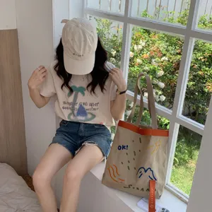 Vue détaillée du sac cabas en toile avec une broderie colorée et des lanières contrastées.