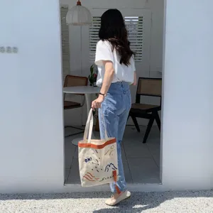 Vue détaillée du sac cabas en toile élégant avec lettres brodées et lanières contrastées.