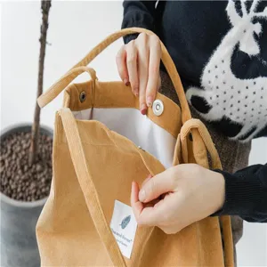 Close-up detail of yellow corduroy tote bag showing magnetic snap button and label.