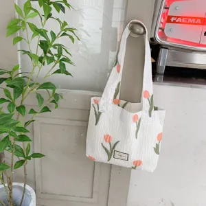 Detailed shot of a white tote bag featuring lovely embroidered pink tulips and green leaves.