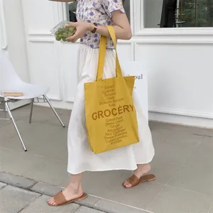 Detail view of yellow canvas tote bag featuring grocery letter and vegetable prints in casual style.