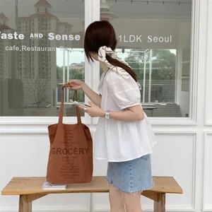 Detailed view of casual brown canvas tote bag featuring grocery lettering print and shoulder strap.