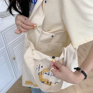 Casual beige canvas tote bag with artistic letter print, interior pocket and snap button closure.