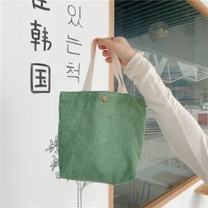 Detail view of a green corduroy mini tote bag, casual daily handbag with white handles.