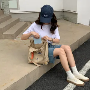 Vue de style urbain montrant un grand sac cabas en toile brodée avec des lanières contrastées.