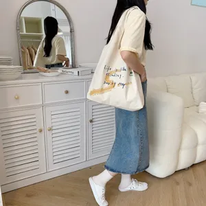 Canvas shoulder bag detail view showing artistic text print and daily indoor lifestyle scene.