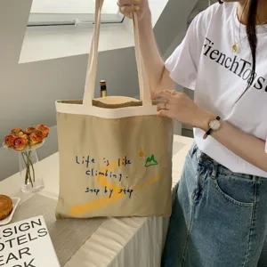 Beige canvas tote bag featuring inspiring English embroidery and mountain graphic detail.