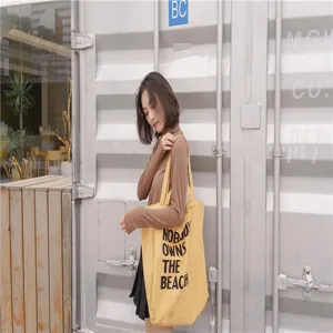 Canvas tote bag detail featuring yellow cotton fabric and black slogan print design.