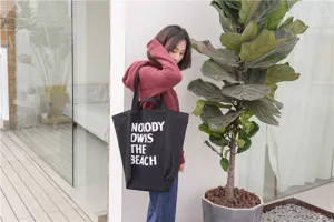 Detail view of black canvas tote bag with letter print, large capacity, casual lifestyle shot.
