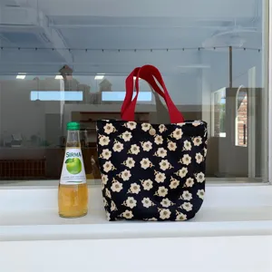 Corduroy lunch handbag featuring a cute white daisy floral print and red handles. Detail shot.