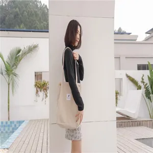 Detailed view of the casual beige canvas tote shoulder bag worn by a model outdoors.