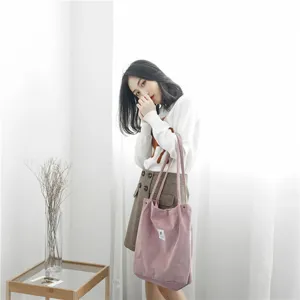 Lifestyle detail shot showing a pink corduroy shoulder tote bag worn by a model in a room.