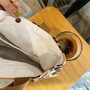 Corduroy lunch bag interior detail showing white lining and snap button on wooden table.