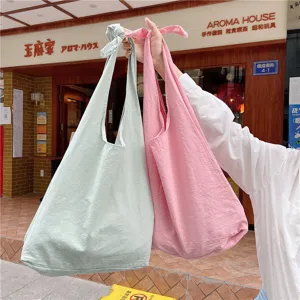 Close-up of canvas vest bags in light green and pink, showing knotted strap detail and fabric texture.