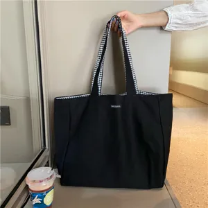 Detail view of the black canvas tote bag showing the dual-sided checkered strap and structure.