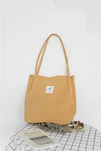 Corduroy tote bag detail showing soft fabric texture, front label, and snap button closure.