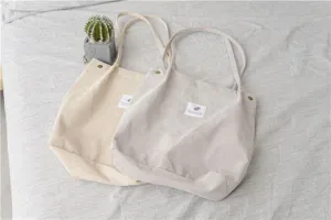 Detail view of corduroy tote bag showing soft fabric texture, metal snap button and label.