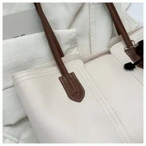 Close-up detail of beige tote handbag featuring contrast brown shoulder straps and chic charm.