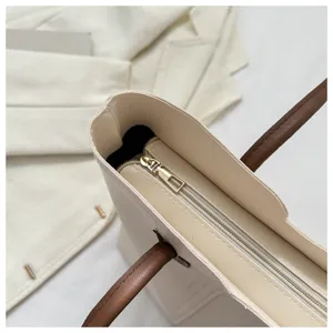Close-up detail of beige tote bag zipper closure and brown handle, elegant minimalist style.