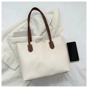 Detail shot of the beige leather tote bag with brown straps, styled on white jacket background.