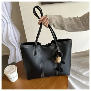 Detailed view of black leather tote bag with contrast stitching and cute sheep pendant on table.