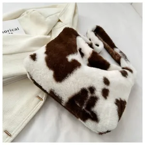 Detail view of a stylish brown and white cow print plush shoulder bag, soft fuzzy underarm handbag.
