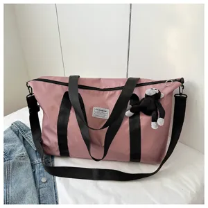 Detail view of pink nylon travel duffel bag with black straps and cute plush monkey keychain.