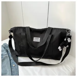 Large black nylon travel tote bag with shoulder strap and cute plush monkey keychain charm.