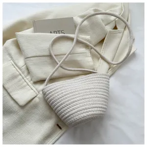 Detailed shot of the woven rope crossbody bucket bag on a white textured fabric background.