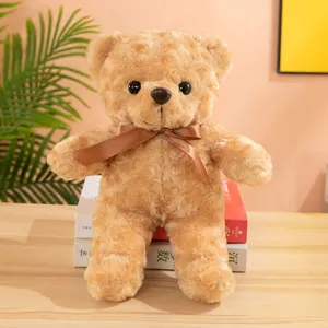 Brown curly plush teddy bear toy with a satin bowknot, displayed on wooden table for detail view.