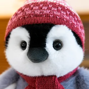 Cute winter penguin plush toy detail shot featuring soft fur, red knitted hat and warm scarf.