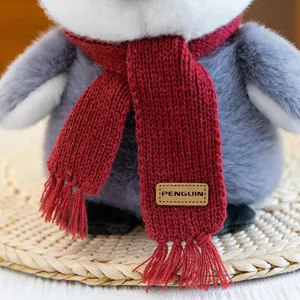 Cute plush penguin toy detail with a red knitted scarf and brand tag for winter cozy gifts.
