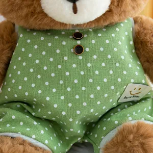 Close-up of cute plush teddy bear wearing green and white polka dot overalls with buttons.