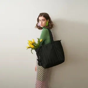 Detailed view of the black quilted puffer tote bag worn by a model holding yellow tulips.