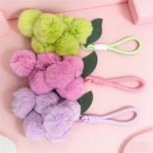 Close-up detail of fluffy plush grape bag charms with green leather leaves and pastel loops.