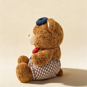Side detail view of a cute brown plush bear toy with a blue beret and checkered shorts.