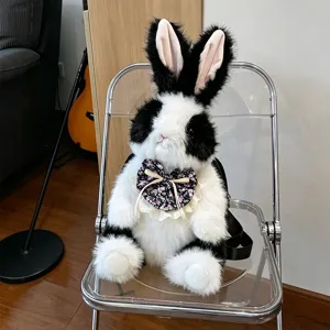 Schattige zwart-witte pluche konijnen pop rugzak met bloemenstrik, zacht speelgoed.