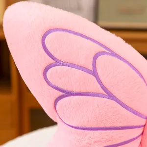 Close-up shot of soft pink plush pillow featuring detailed purple embroidered wing patterns.