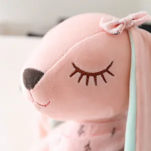 Close-up detail of cute pink plush rabbit toy with closed eyes embroidery and bow.