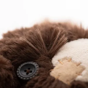 Close-up detail shot of cute brown teddy bear plush toy featuring button eye and patch design.