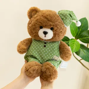 Cute brown plush teddy bear wearing green polka dot pajamas and sleeping hat, soft detail view.