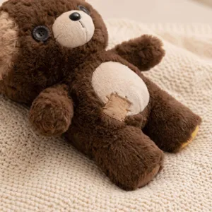 Cute brown plush teddy bear detail showing button eyes and belly patch on knit blanket.
