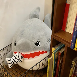 Detailed close-up of cute grey shark plush toy biting a small fish doll in a wire basket.