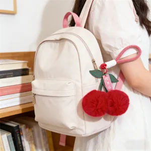 Casual beige backpack with pink straps and cute red fluffy cherry pom pom charm for daily.
