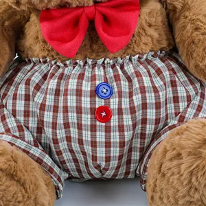Close-up detail of cute plush teddy bear with red bow tie and plaid shorts, soft texture.