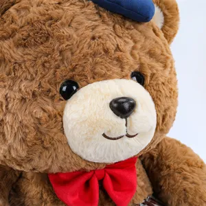 Close-up of brown plush teddy bear detail showing soft fur, blue hat and red bow tie.