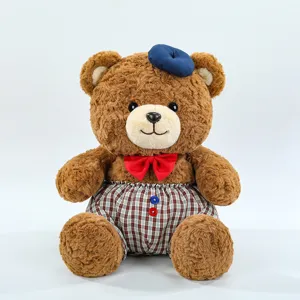 Cute brown teddy bear plush toy wearing a blue beret and red bow tie with plaid shorts.